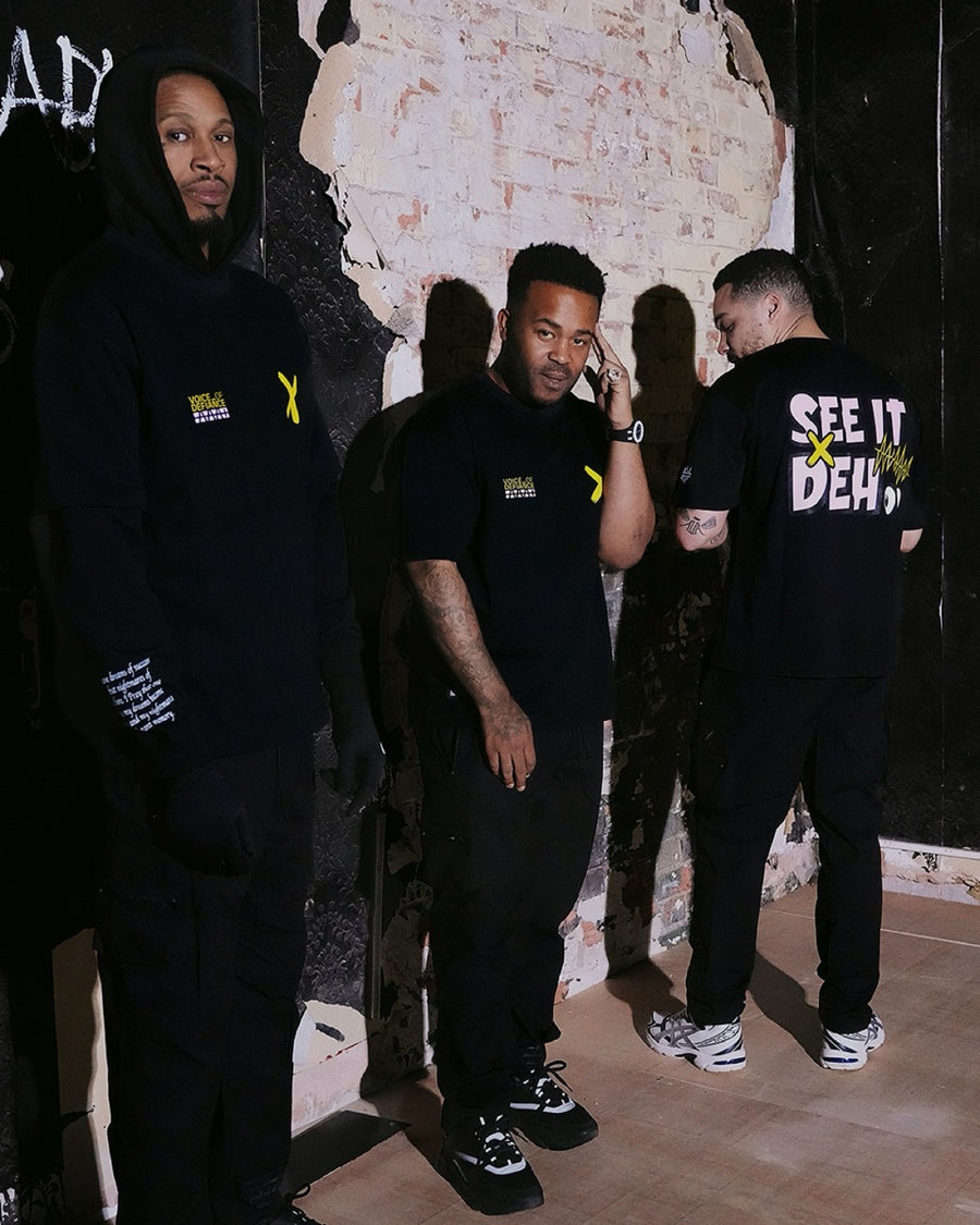 Three of the crew against a torn brick wall, one showing the back print.