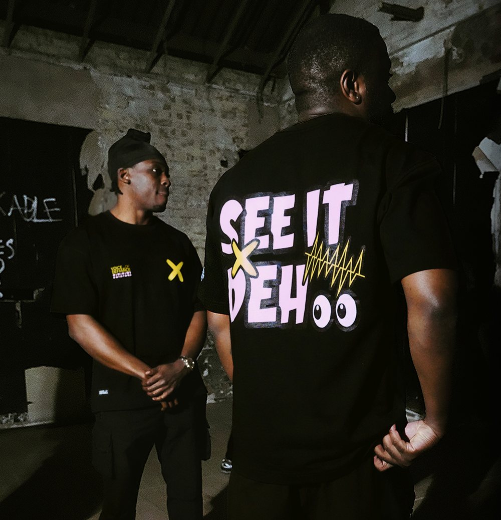 Night shoot: two of the collective in a derelict room, one turned to show the SEE IT DEH back print.